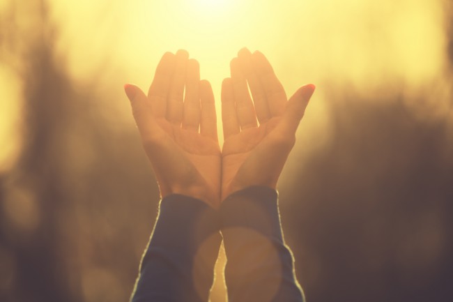 doua maini in pozitia de rugaciune luminate de razele soarelui