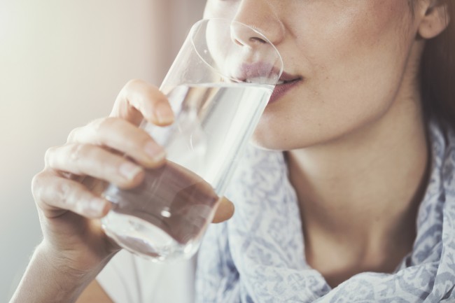 femeie care bea un pahara de apa pentru a se hidrata