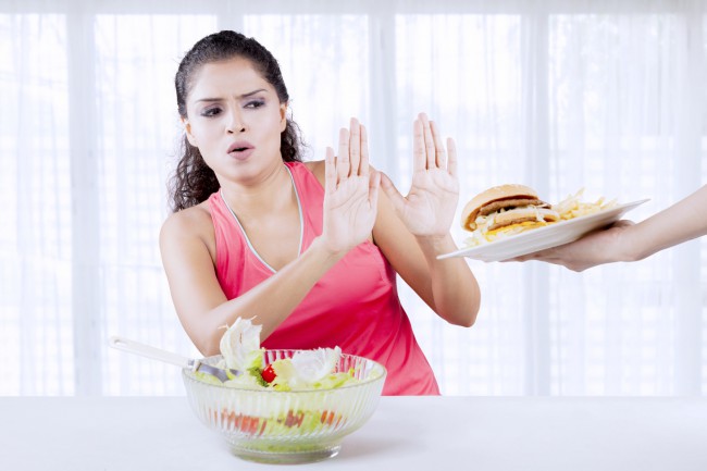 Femeie care refuză un burger și are o salată în față