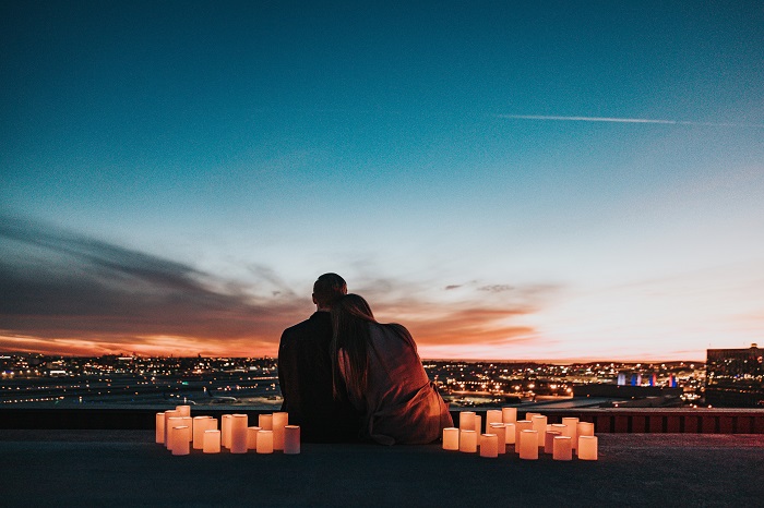 Cuplu de tineri înconjurați de lumânări în timp ce admiră orașul pe înserate