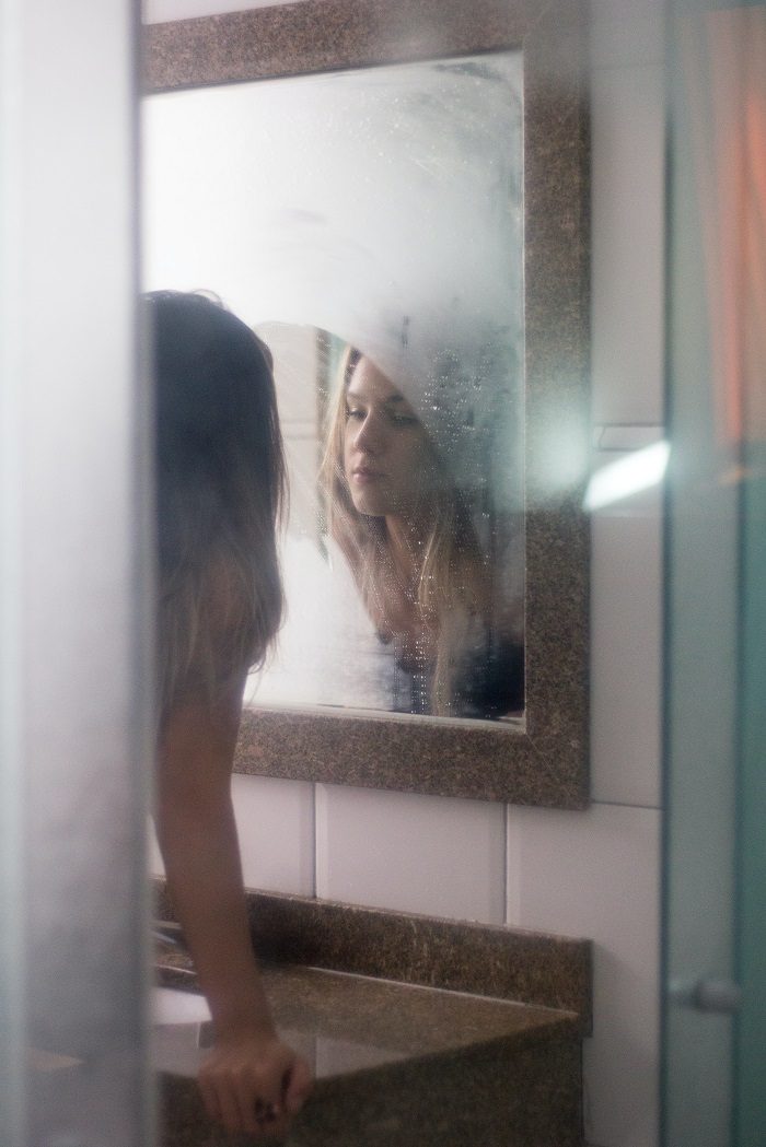 Tânără privindu-se la reflecția ei într-o oglindă aburindă