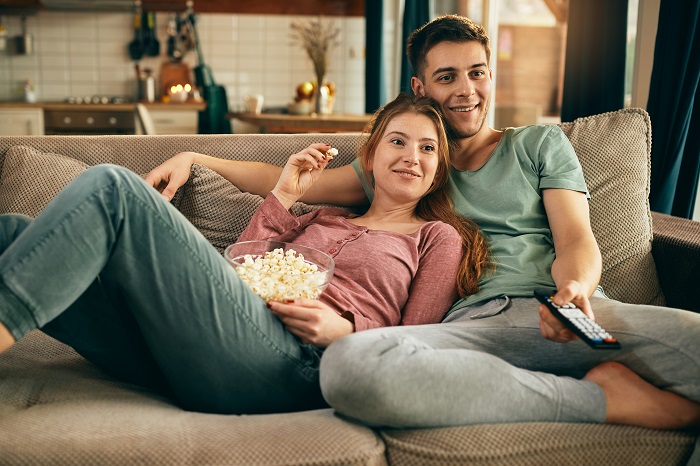 cuplu care se uita la un film cu un bol de popcorn in mana