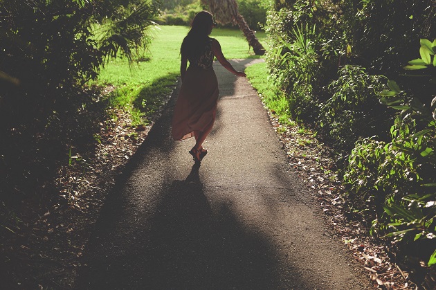 Femeie îmbrăcată într-o rochie văratică plimbându-se pe o alee însorită și plină de plante 