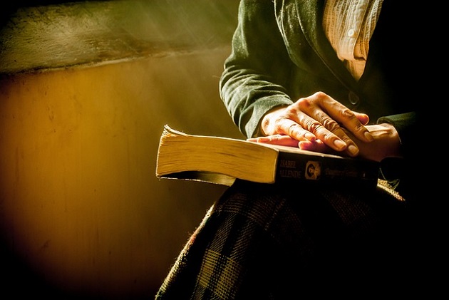Femeie care se roagă lângă fereastra ținând Biblia pe picioare