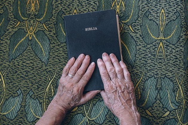 Mâinile unei bunicuțe pe Biblie în timp ce se roagă 