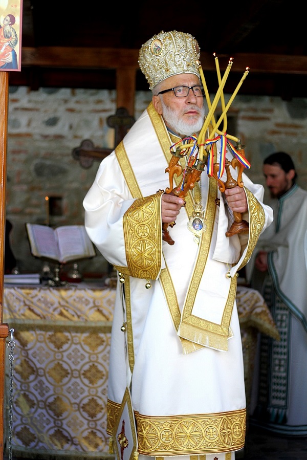 arhiepiscopul muscelului și argeșului ține în mână mai multe lumânări aprinse cu semnul tricolorului în biserică