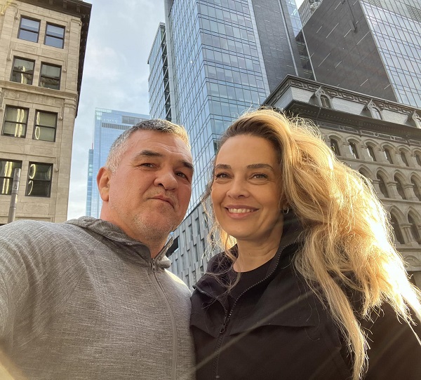 leonard doroftei in pulover crem alaturi de sotia lui blonda monica in spate blocuri zgarie nori