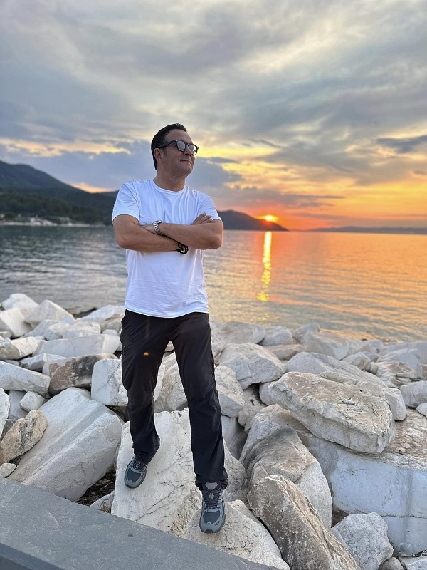 daniel buzdugan asezat in picioare pe pietre cu un apus in spate in mare