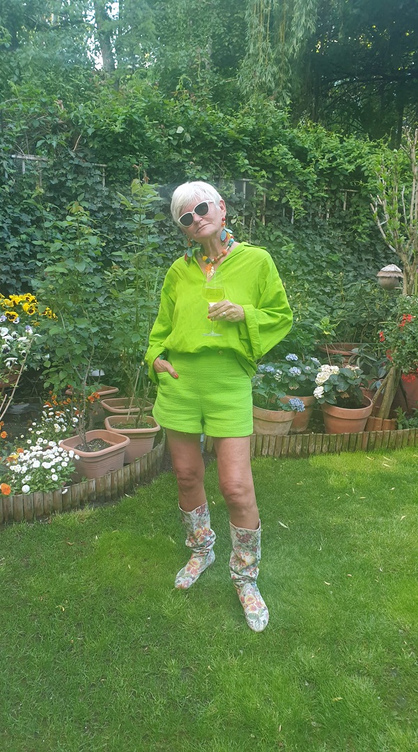 monica tatoiu imbracata in verde cu cizme albe in picioare intr-un decor verde