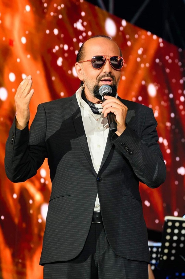 daniel iordachioae imbracat in costum cu ochelari desoare canta pe scena cu microfon in mana