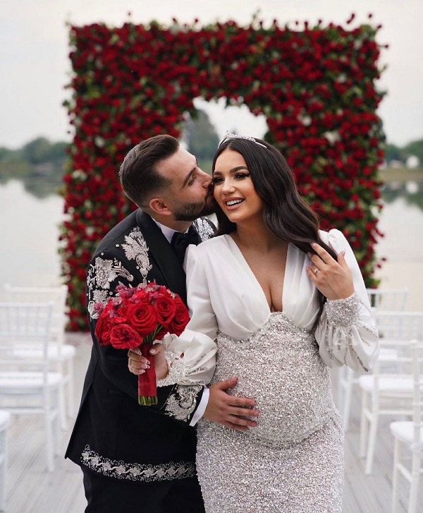 larisa udina insarcinata in rochie alba sotul ei ii tine mana pe burta pe malul unui lac