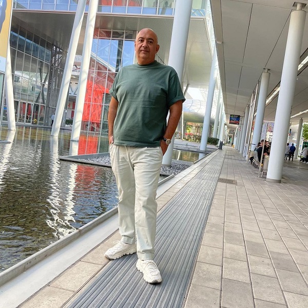 robert batlan in pantaloni albi si bluza kaki sta cu mainile in buzunare