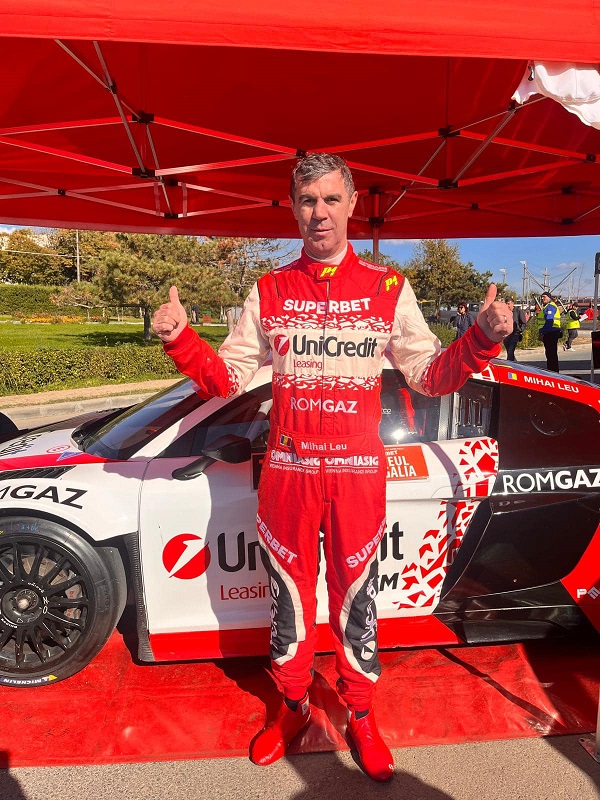 mihai leu imbracat in costum de raliu langa o masina de curse rosie