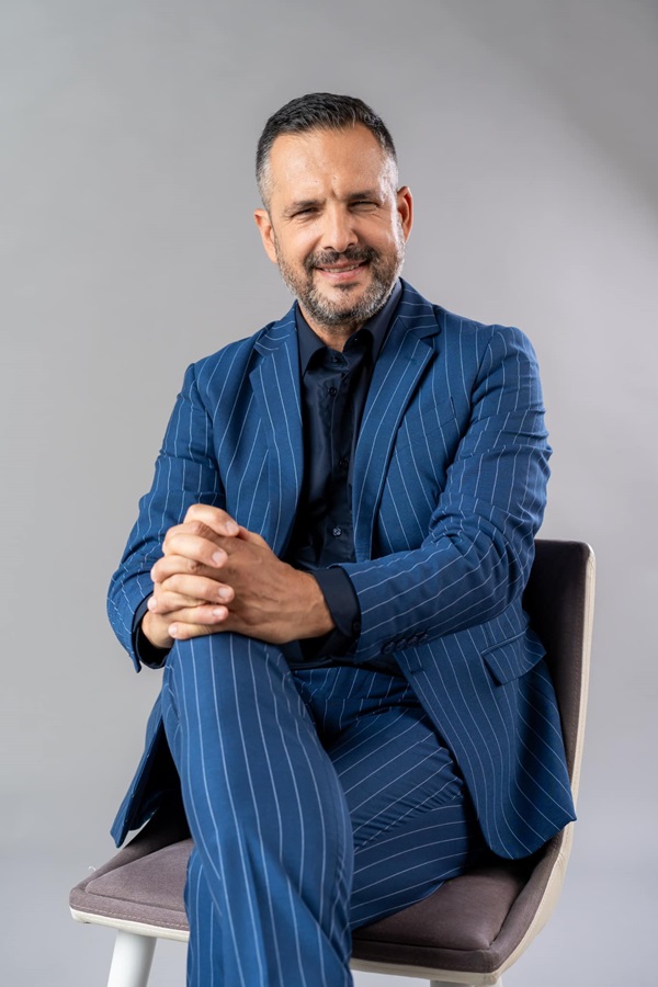 madalin ionescu imbracat in costum albastru sta picior peste picior pe un scaun