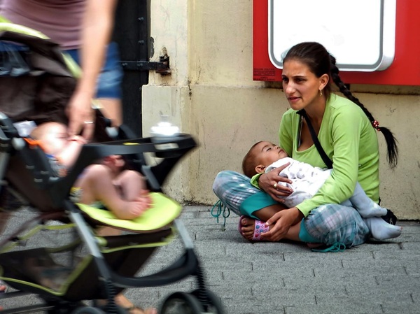 persoana de etnie roma cu bebelus in brate cere pe marginea drumului bani
