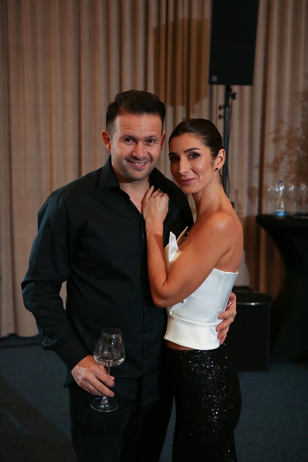 robert tudor alaturi de sotia sa tine un pahar in mana si o imbratiseaza