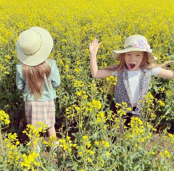 fetite gemene cu palarii pe cap in lanul de rapita fac poze