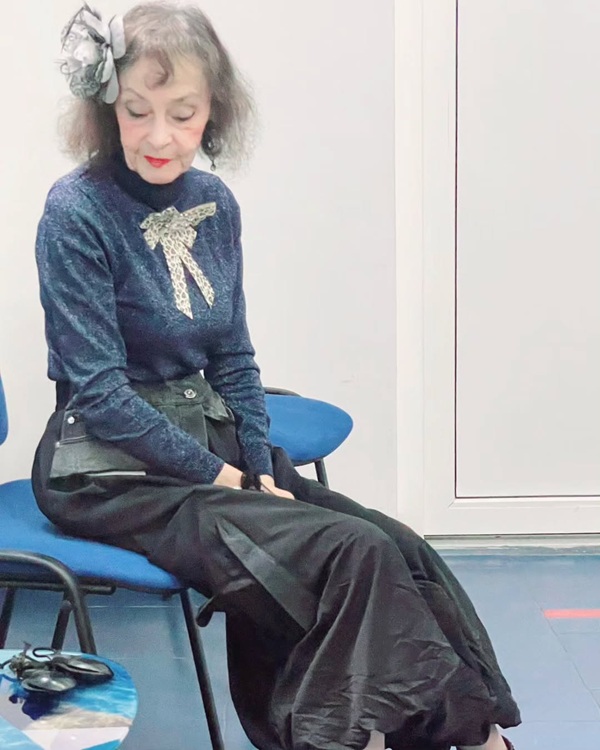 marina voica imbracata in camasa bleumarin si o fusta lunga sta pe un scaun cu privirea in jos