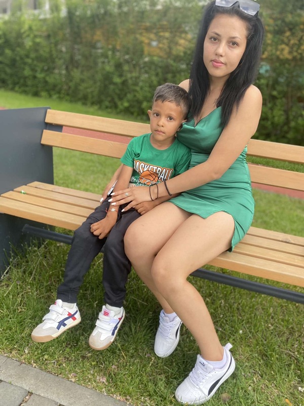 femeie bruneta imbracata in rochie scurta verde sta pe banca cu un baiat