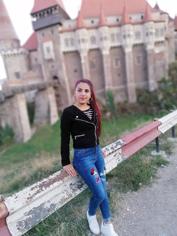 femeie in blugi si hanorac negru sta sprijinita de un gard de piatra