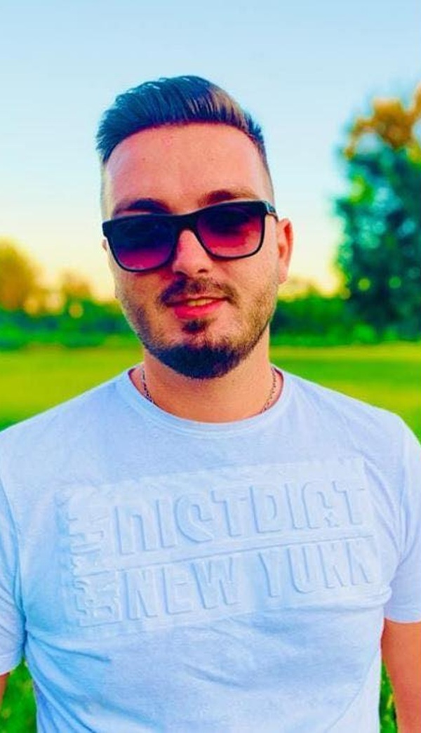 barbat cu barba si mustata cu ochelari de soare la ochi imbracat in tricou bleu pe o pajiste