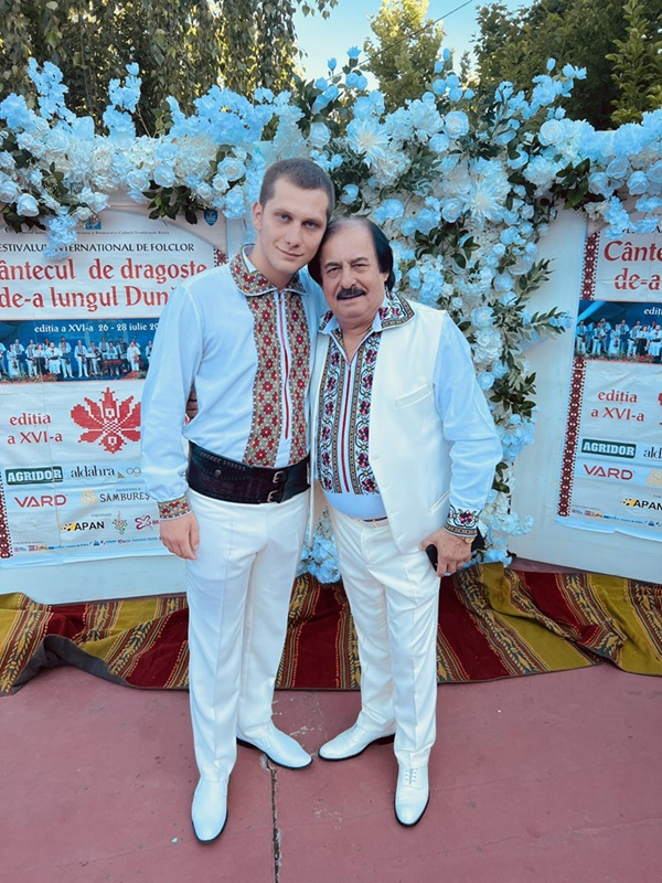 nicolae si cristian botgros in costum popular alb in fata unui panou cu flori