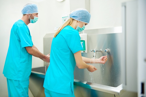 doi asistenti medicali imbracati in halate albastre se spala pe maini la chiuvetă