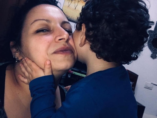 mama bruneta cu parul prins in coada este pupata pe obraz de fiul ei