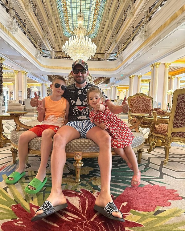 dragos grigore in pantaloni scurti si papuci isi tine copiii in brate