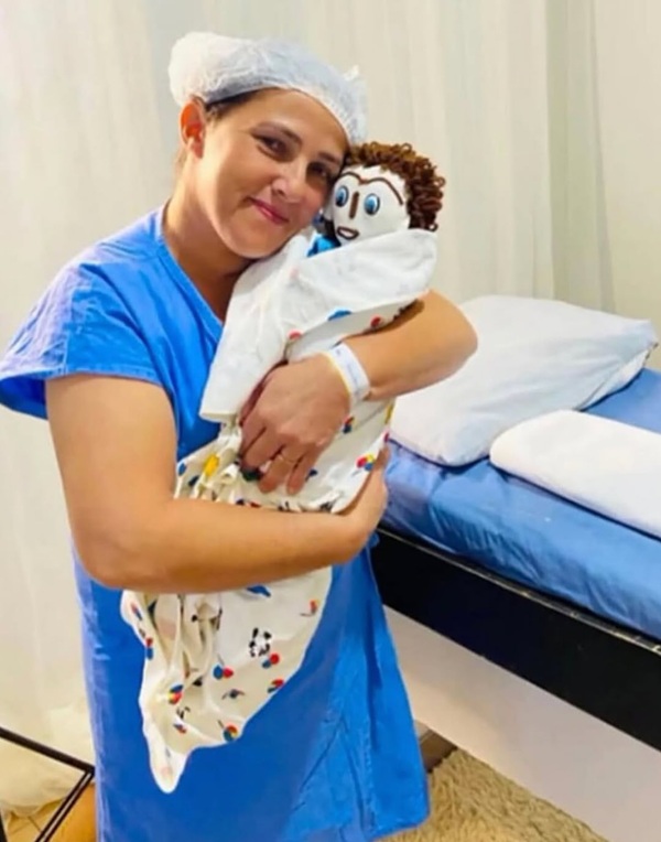 femeie imbracata in albastru cu boneta pe cap tine o papusa de carpe in brate