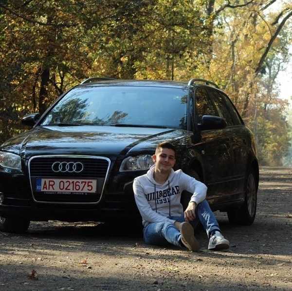 baiat in hanorac alb si blugi sta langa o masina neagra