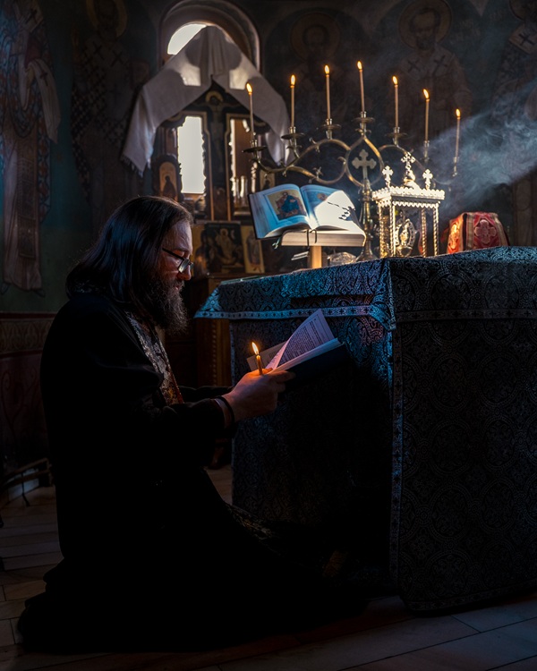 parintele dan damaschin ingenuncheat in biserica cu o lumanare si o carte in mana