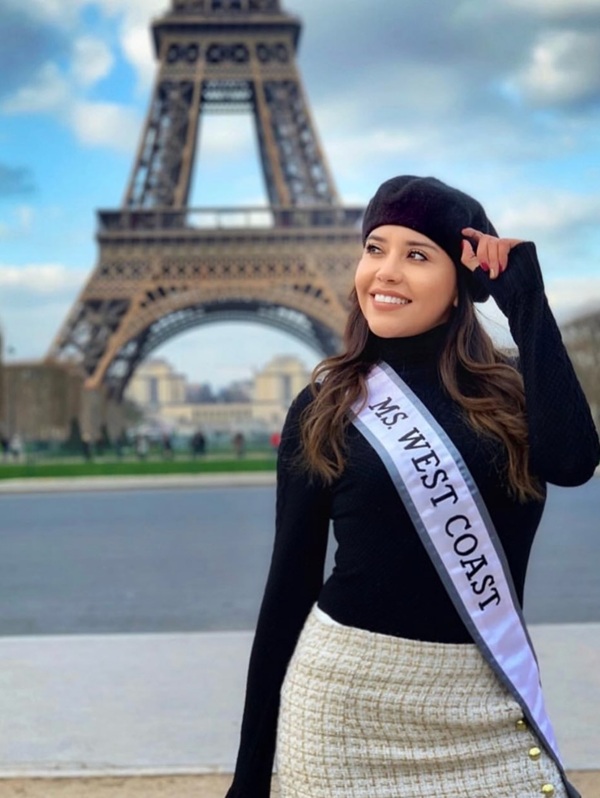 femeie cu titlu de miss face poza tinandu-se de bereta langa turnul eiffel