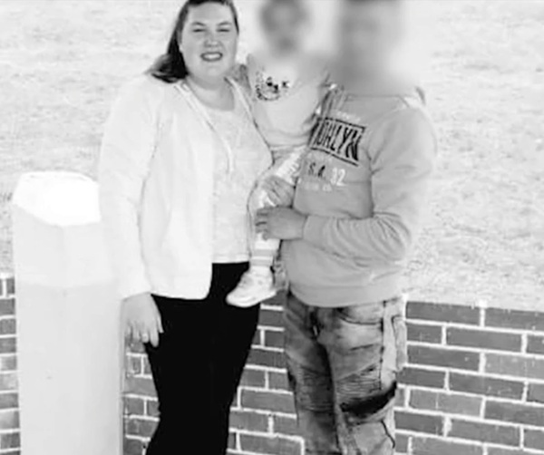 fotografie cu o mama imbracata in bluza alba si pantaloni negri care isi tine fiica in brate langa sotul ei