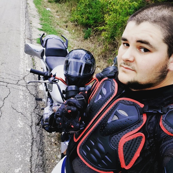 baiat cu barba si mustata isi face selfie langa o motocicleta cu casca in mana