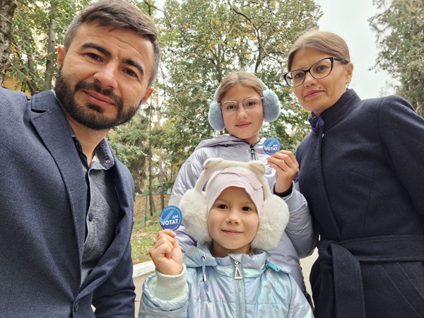 ludmila vartic cu ochelari de vedere imbracata in palton negru dumitru vartic si copilele lor care tin in mana hartii pe care scrie am votat fac un selfie