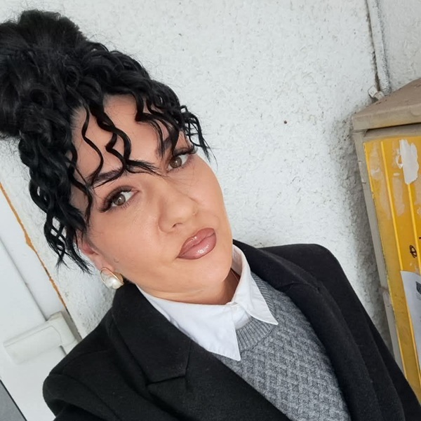 femeie cu parul brunet prins in coc cret imbracata in costum negru cu machiaj