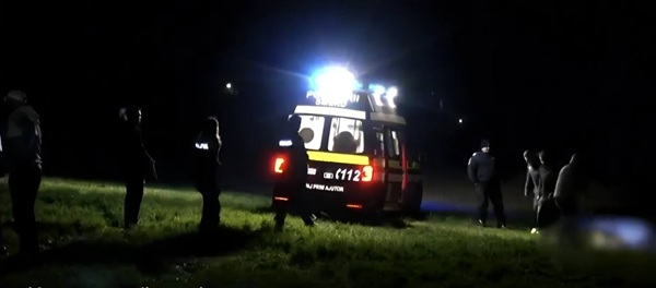 o ambulanta oprita pe un camp cu luminile pornite incojurata de ambulantieri