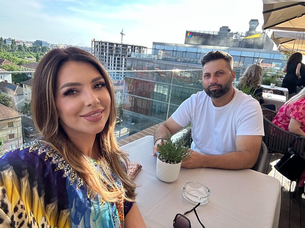 celia imbracata intr-o bluza colorata face un selfie in timp ce sta cu sotul ei la masa