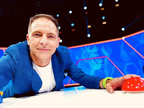 dan negru imbracat in sacou albastru si tricou alb face un selfie din platoul unei emisiuni