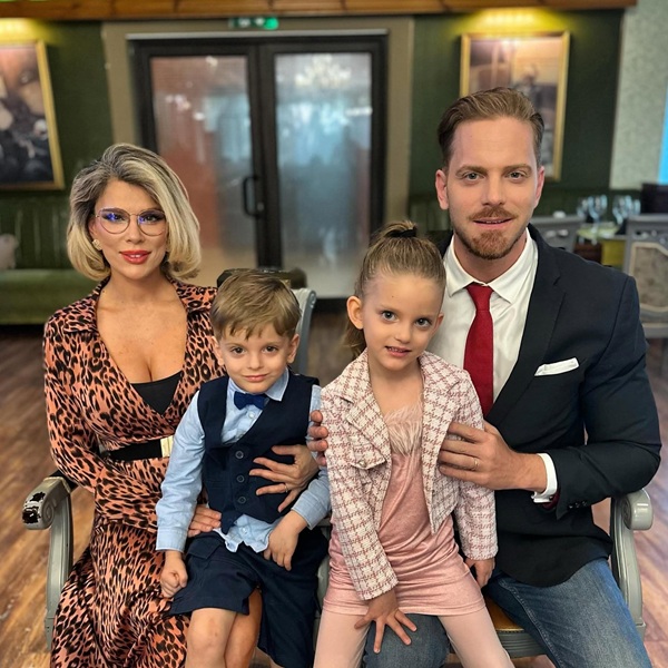 alina laufer imbracata in rochie maro ilan laufer in costum negru isi tin copiii in brate stand pe scaune