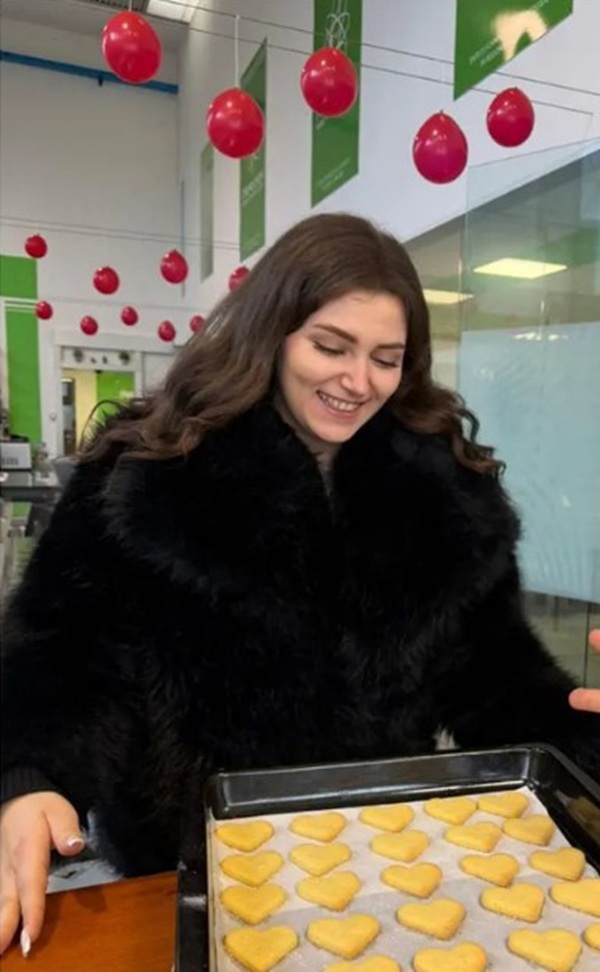 femeie satena cu parul lung imbracata in haina de blana neagra priveste un platou cu prajituri in forma de inima