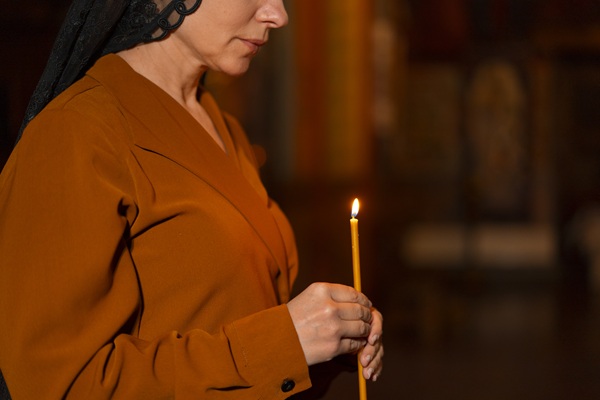 femeie cu bluza maro tine o lumanare in mana in biserica