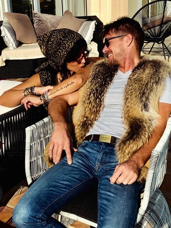 mihaela radulescu imbracata in maiou cu imprimeu leopard cu un batic in cap ii saruta umarul partenerului sau care sta pe scaun si are o vesta de blana