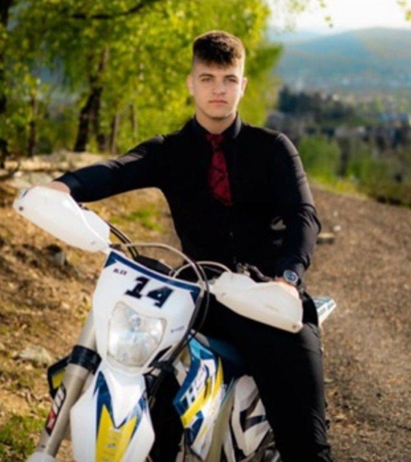 baiat in costum negru langa o motocicleta in natura