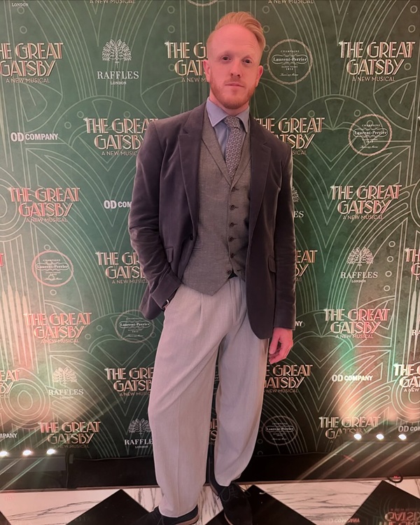 actorul din twin peaks imbracat in pantaloni gri cu palton negru in fundal un panou cu the great gatsby