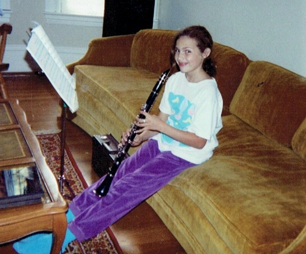 fata imbracata in bluza alba cu pantaloni mov pe o canapea canta la un instrument