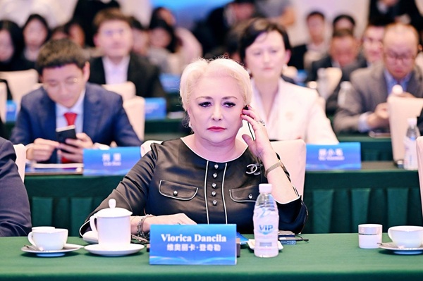 viorica dancila imbracata in negru cu o ceasca de cafea si o sticla de apa in fata la o intrunire importanta tine mana pe casca din ureche