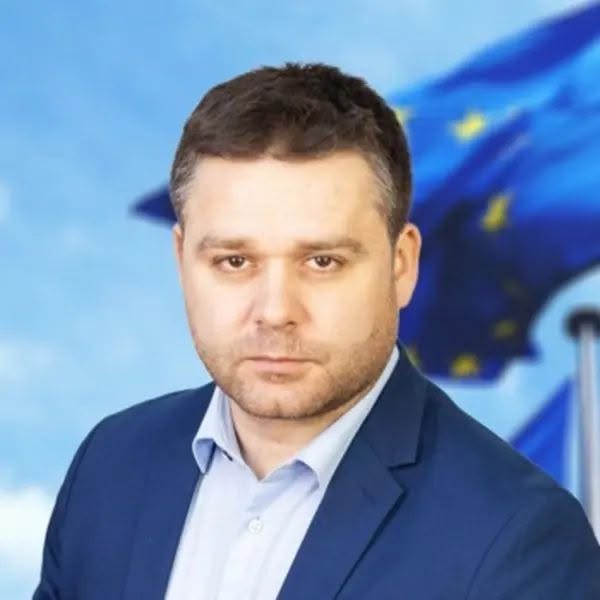 ciprian ciucu in costum albastru pe fundal steagul UE