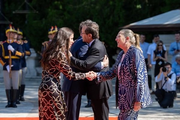 mirabela gradinaru in rochie midi maro cu motive aurii da mana cu prima doamna a poloniei imbracata in albastru